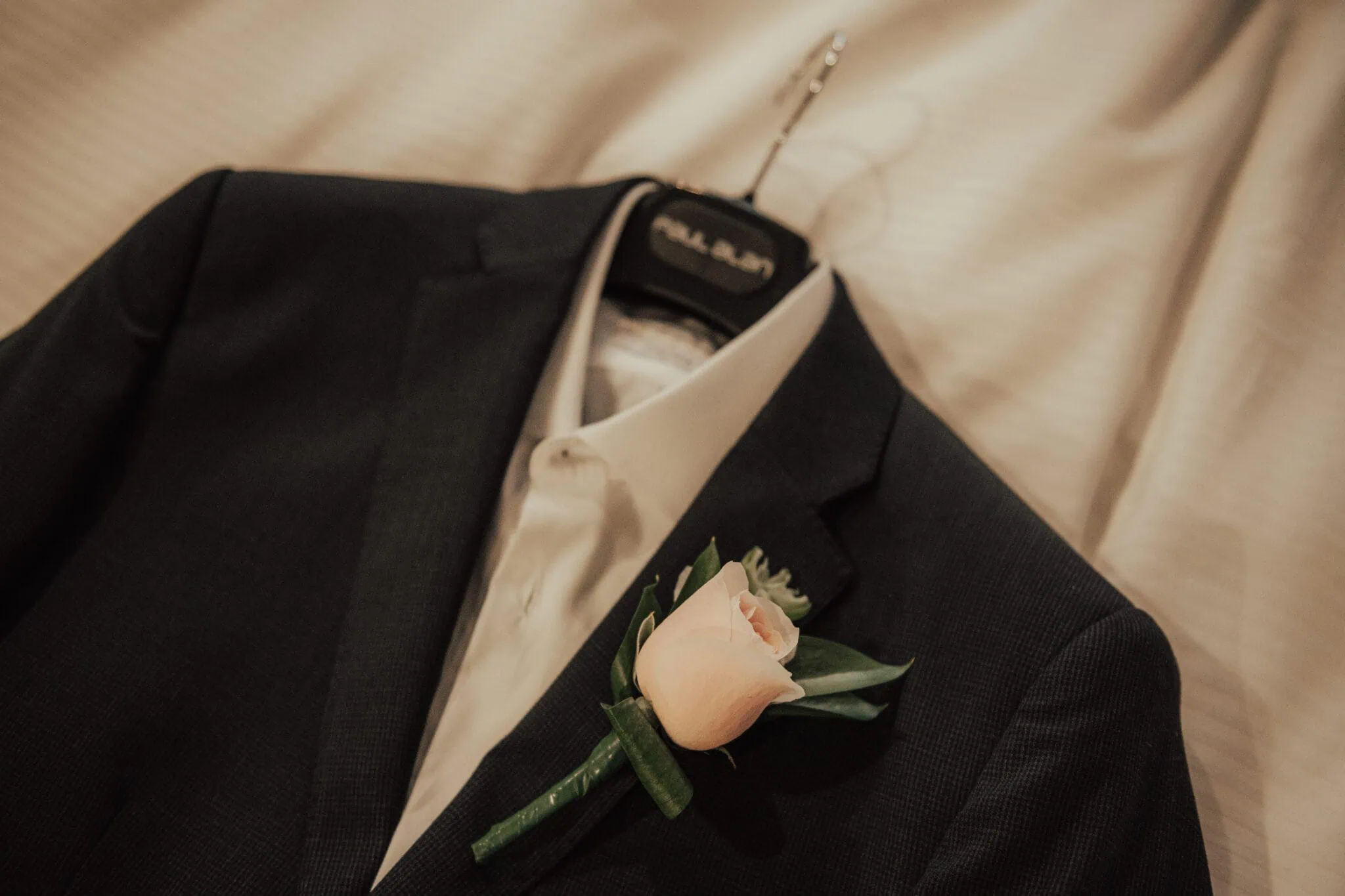 queenstown new zealand heli wedding elopement photographer videographer | For Chloe & Jimmy's elopement wedding in Queenstown, a dark suit jacket on a hanger, with a white shirt underneath, is adorned with a light pink rose boutonniere.