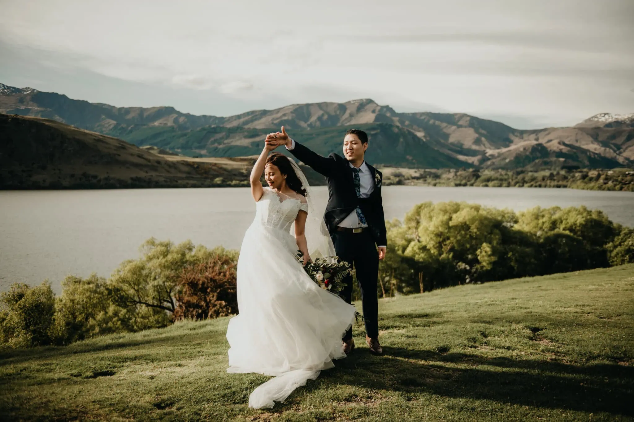 queenstown new zealand heli wedding elopement photographer videographer | Bride and groom dancing outdoors in a scenic mountainous landscape with a lake and green hills in the background at the stunning Stoneridge Wedding venue in Queenstown, NZ.