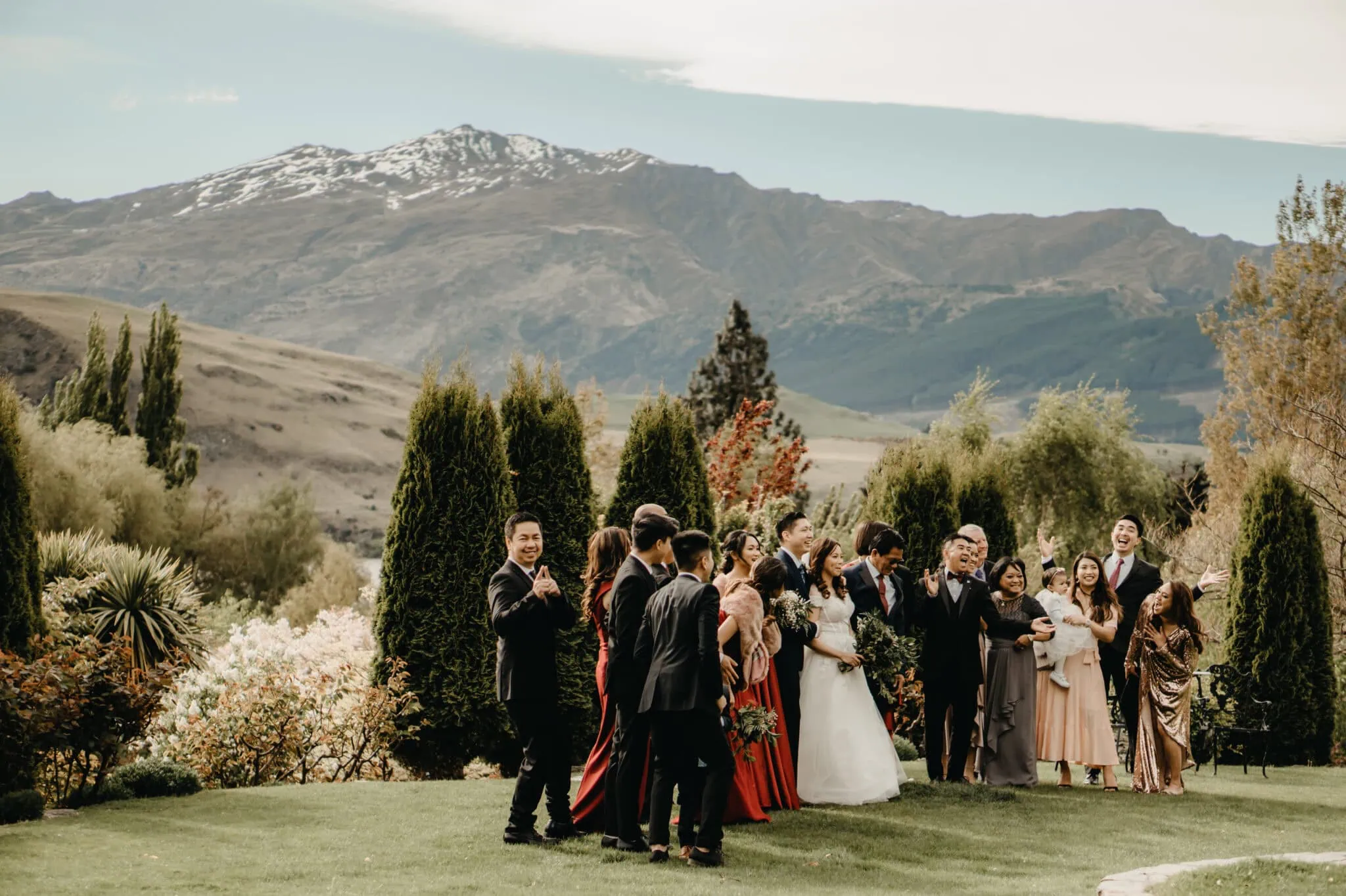 queenstown new zealand heli wedding elopement photographer videographer | A wedding party poses for a photo in an outdoor setting in Queenstown NZ, surrounded by greenery and mountains in the background. The group includes the bride, groom, and several guests. This beautiful Stoneridge Wedding captures the joy of Natalya & John’s special day.