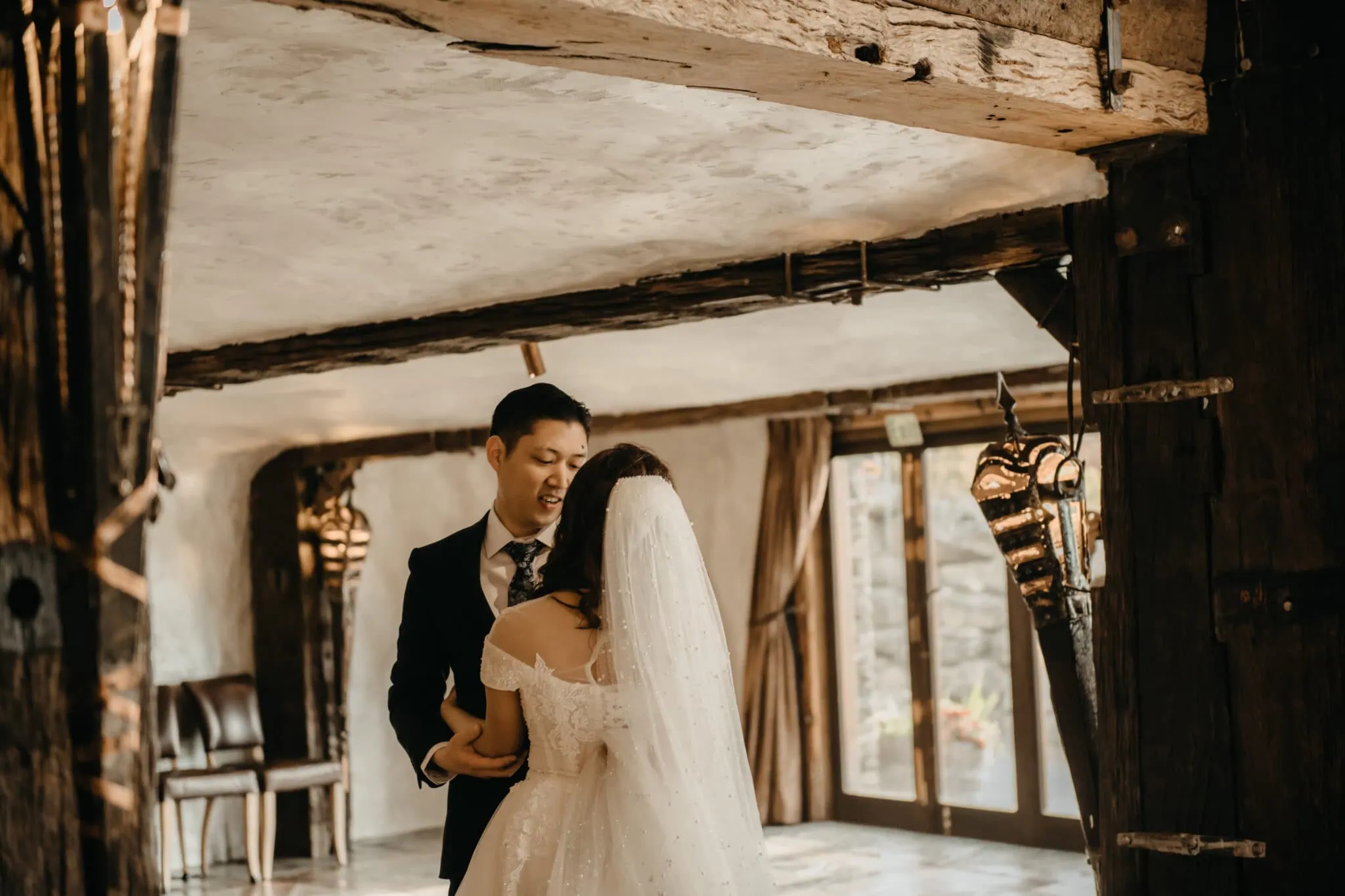 queenstown new zealand heli wedding elopement photographer videographer | A bride and groom share a moment together in a rustic indoor setting with timber beams, a wedding dress, and a dark suit at their Stoneridge Wedding in Queenstown NZ.