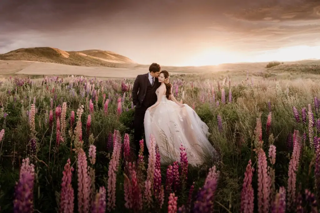 A bride and groom are standing in a field of flowers, in Tekapo for their Pre-Wedding Photoshoot in New Zealand