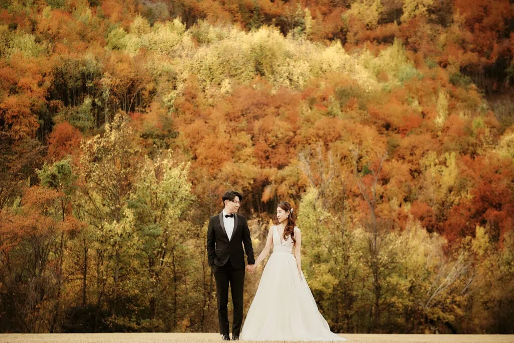 queenstown new zealand heli wedding elopement photographer videographer | A couple in wedding attire stands hand in hand, with an autumn forest of red, orange, and yellow foliage as the backdrop during their Heli Pre-Wedding Shoot in Queenstown, NZ.