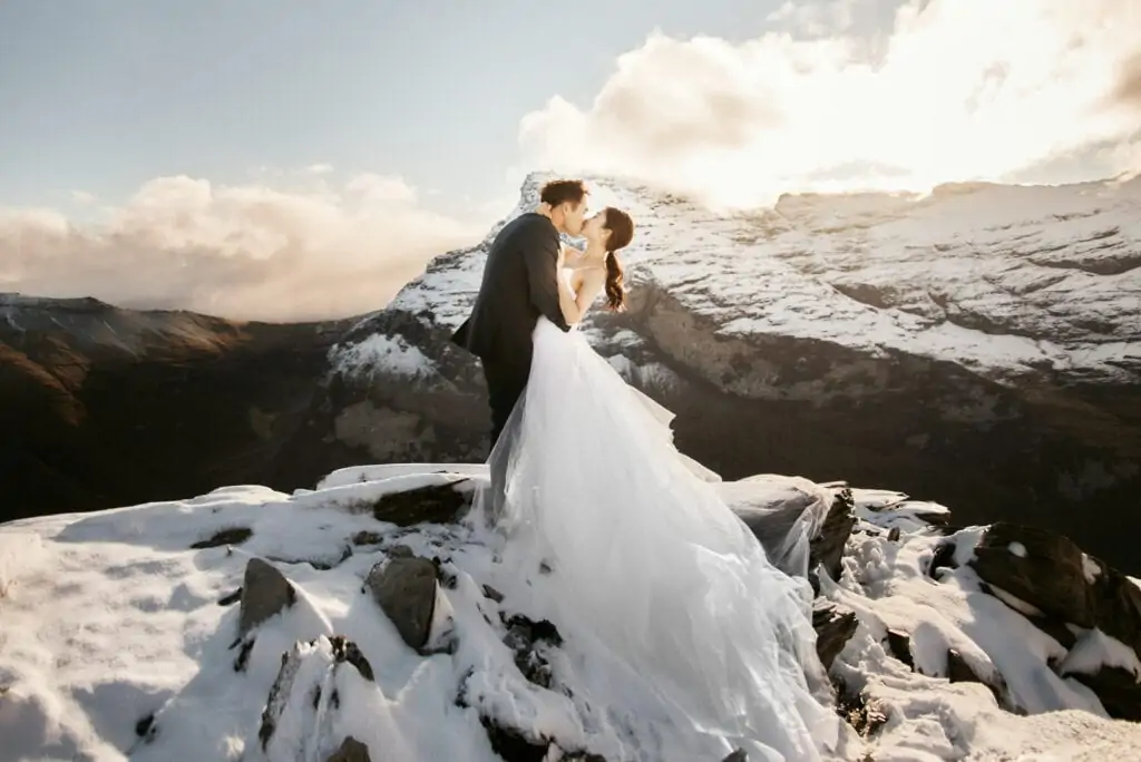 A queenstown bride and groom standing on top of a snow covered mountain.