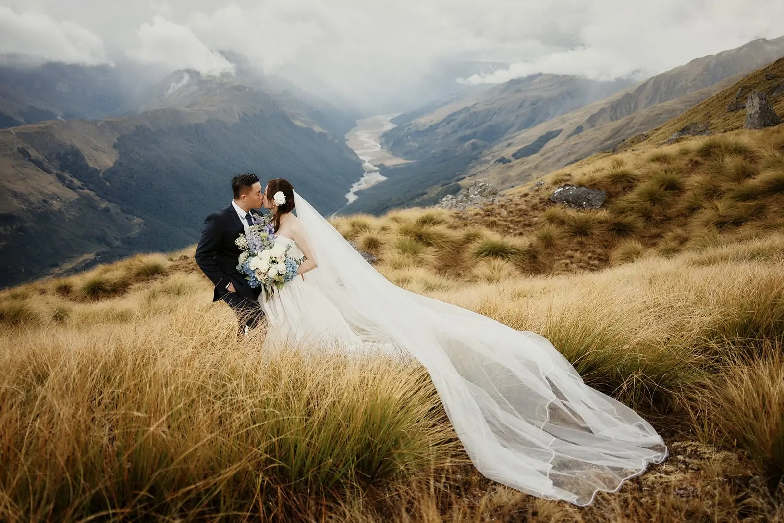 A bride and groom standing on top of a mountain in new zealand.