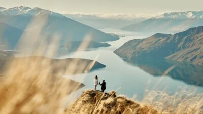 Two people standing on top of a mountain in New Zealand overlooking Lake Wanaka.