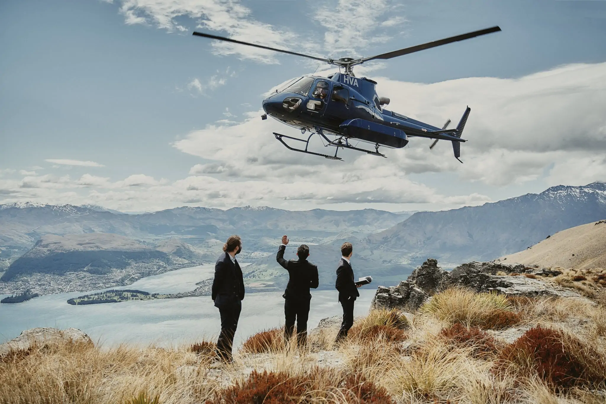 A helicopter safely hovers over a group of people on top of a mountain.