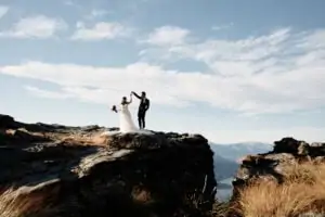 Tomomi Ito - Portfolio featuring a bride and groom on a cliff overlooking mountains.