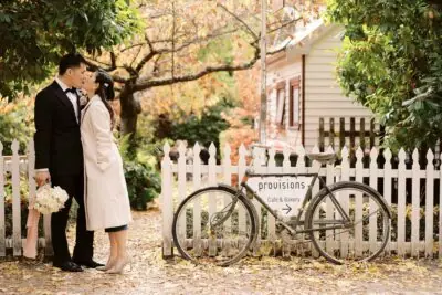 Ayaka Morita captures a loving moment between a bride and groom in front of a white picket fence for her portfolio.
