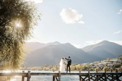 A bride and groom on a dock in front of mountains, Tracy & Markus' Cecil Peak Heli Wedding Previews.