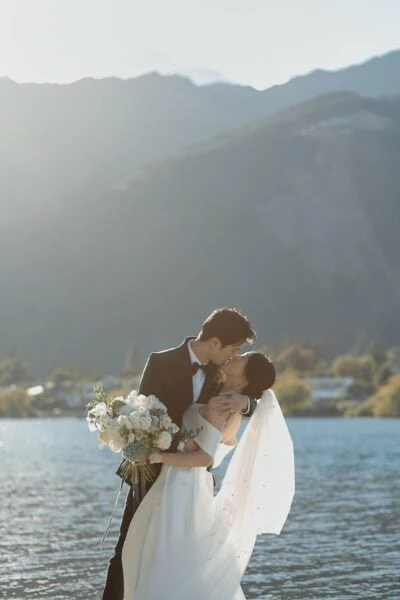 Tracy & Markus' Cecil Peak Heli Wedding Previews: A newlywed couple shares a romantic kiss by Lake Wanaka.