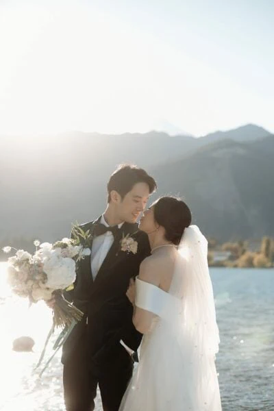 Ayaka Morita's portfolio featuring a bride and groom posing by a lake with mountains in the background.