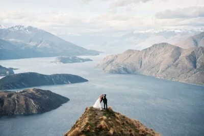 Queenstown New Zealand Elopement Wedding Photographer - Ayaka Morita's portfolio showcases a breathtaking image of a bride and groom standing on top of a mountain, overlooking Lake Wanaka.