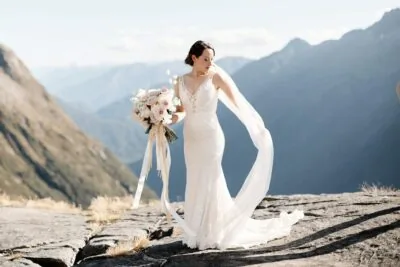 An elopement wedding photographer captures a bride standing on top of a mountain with her veil in Queenstown, New Zealand.