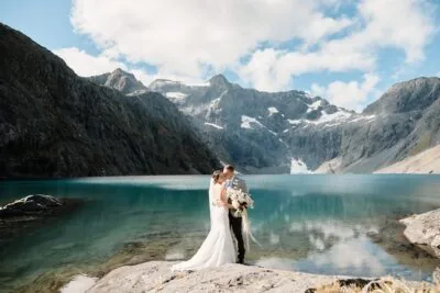 A Queenstown newlywed couple posing in front of a scenic lake for their elopement wedding photographs.