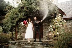 Josh Yates - Portfolio: Capturing a playful moment between a bride and groom as they spray water on each other in front of a house.