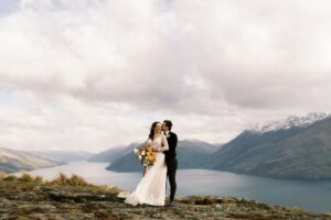 Queenstown New Zealand Elopement Wedding Photographer - photograph of a bride and groom standing on top of a mountain overlooking Lake Wakatipu, at Deer Park Heights