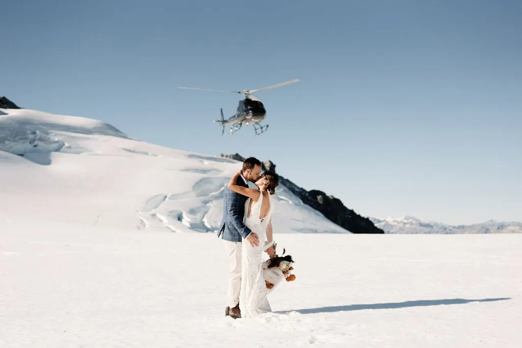 A bride and groom posing in front of a helicopter, featured in Josh Yates' photography portfolio.