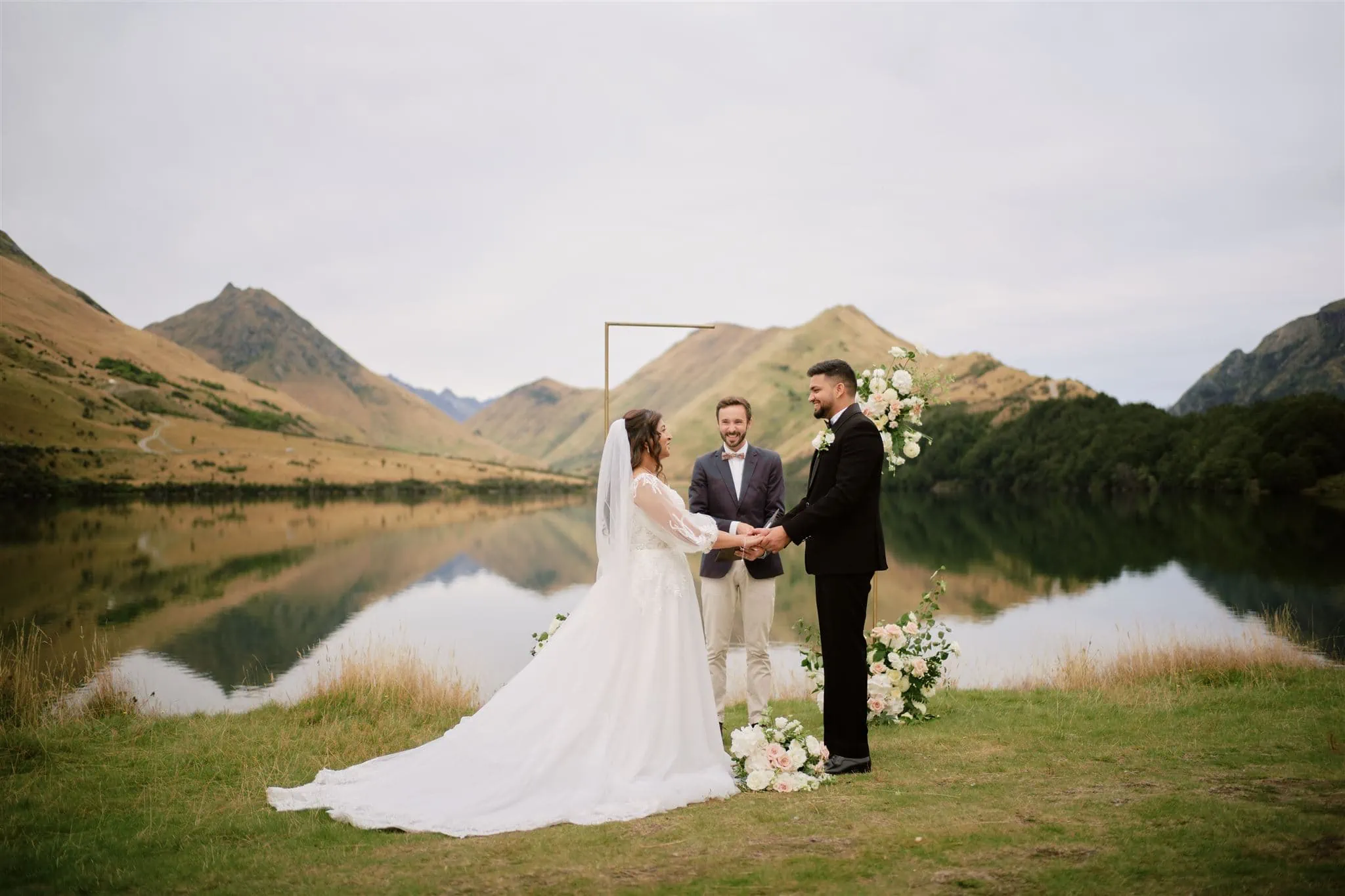 Queenstown New Zealand Heli Wedding Elopement Photographer クイーンズタウン　ニュージーランド　エロープメント 結婚式 | A couple exchanging vows at a lakeside wedding ceremony with a scenic mountain backdrop at Moke Lake, Queenstown.
