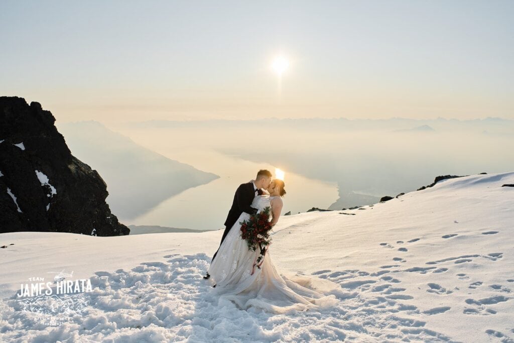A Queenstown Wedding Photographer captures a bride and groom kissing on top of a snow covered mountain.
