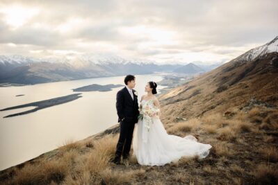 A couple in Queenstown, New Zealand, having a pre-wedding shoot with a photographer on top of a mountain overlooking Lake Wakatipu, on Mt Creighton