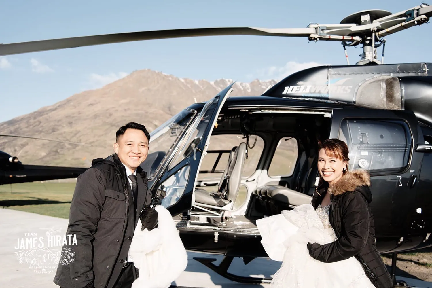 Joan and Brandon, a bride and groom, standing next to a helicopter in Queenstown.