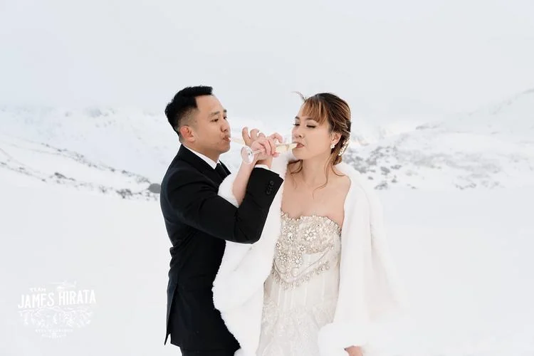 Joan and Brandon share a bottle of wine during their Queenstown Heli Pre Wedding Shoot in the snow.