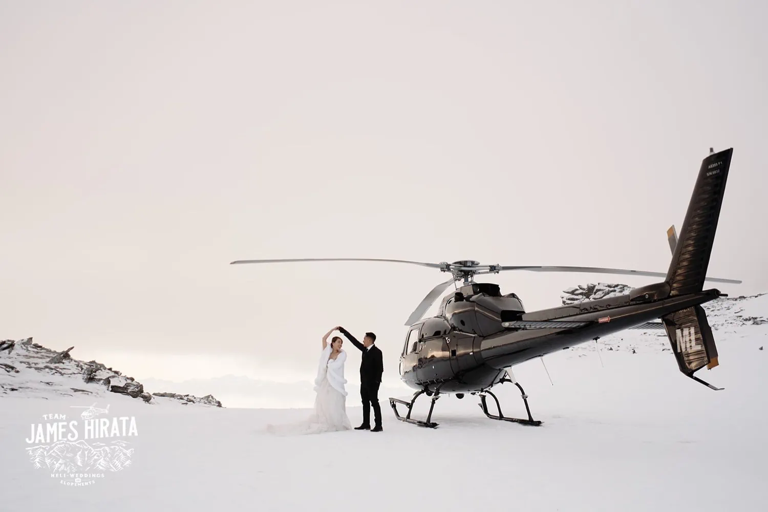 Joan and Brandon posing next to a helicopter in the snow during their Queenstown Heli Pre Wedding Shoot.