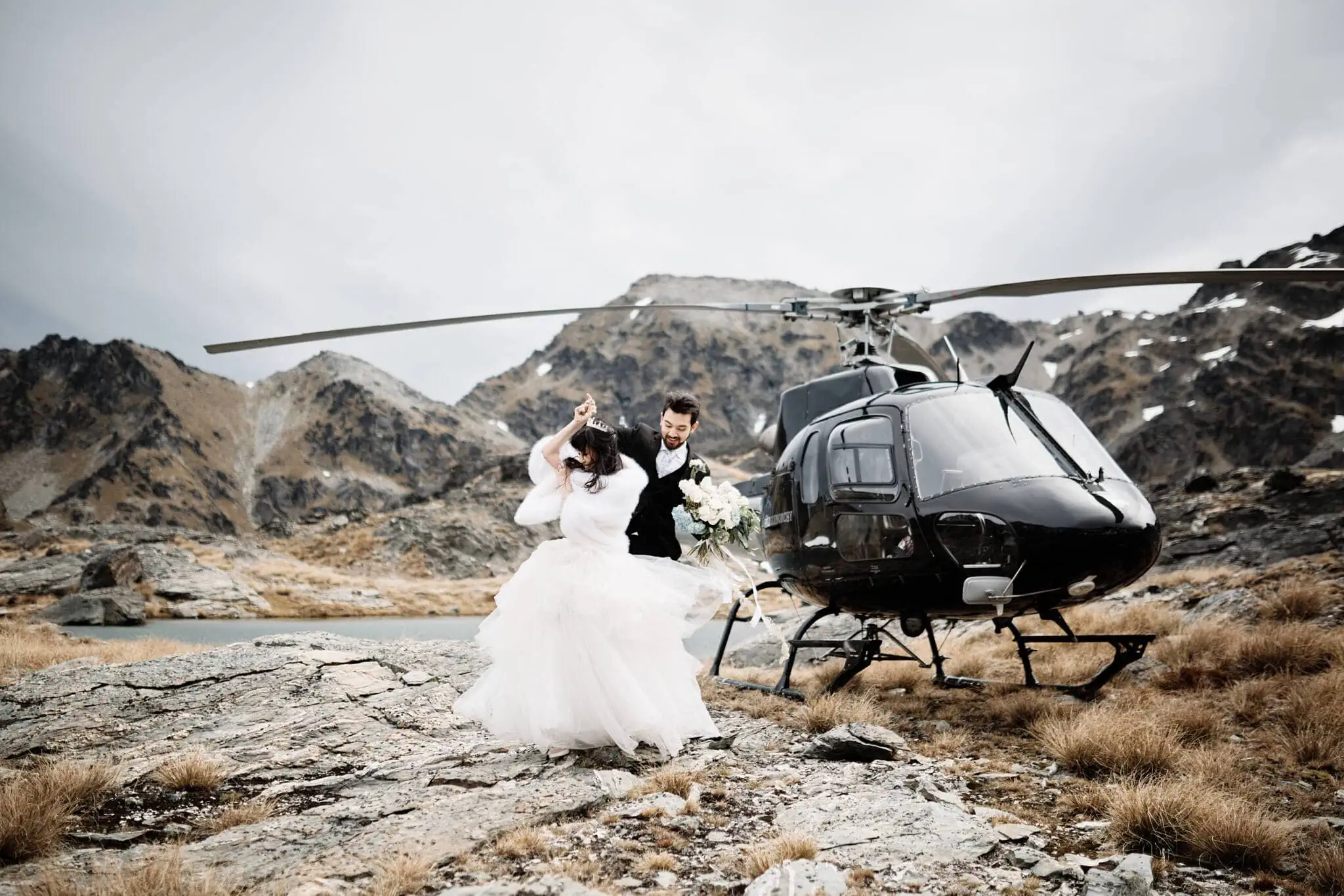 Carlos and Wanzhu embrace on their intimate Cecil Peak Heli Elopement Wedding day, standing next to a helicopter.