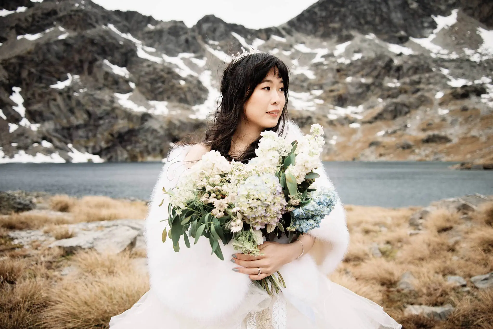 Carlos and Wanzhu's intimate heli elopement wedding with a bride holding a bouquet in front of Cecil Peak mountains.