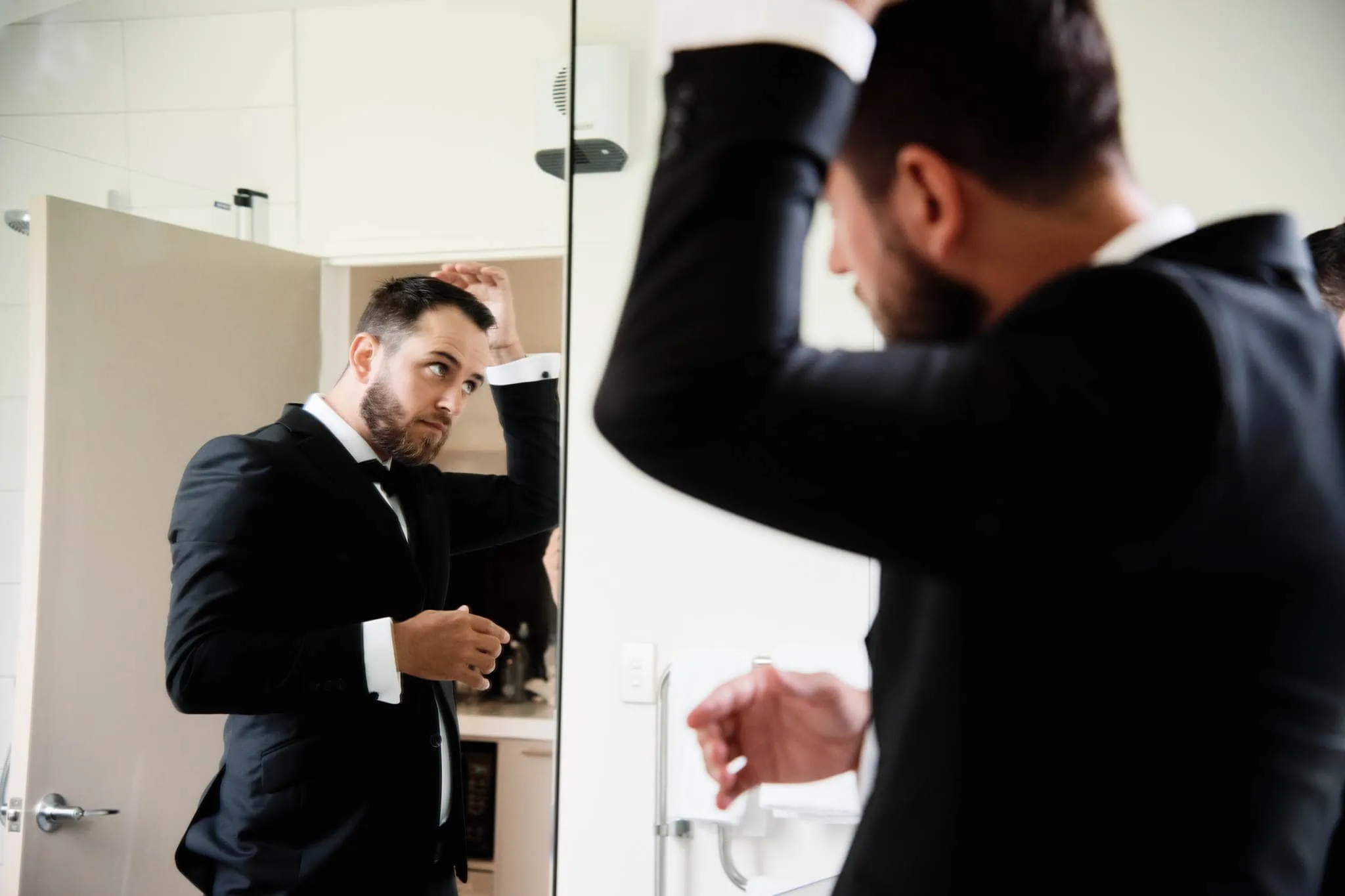 A man in a tuxedo is adjusting his hair in front of a mirror during his Sapphire and JJ Queenstown Heli Elopement Wedding.