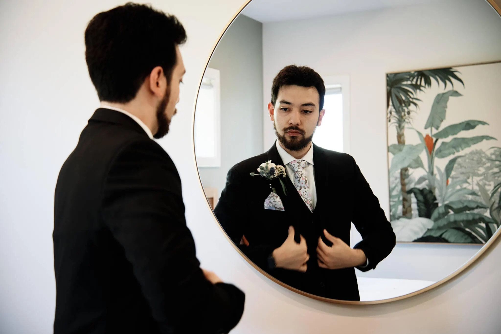 Carlos, in a suit, is putting on his tie in front of a mirror for his intimate Cecil Peak Heli Elopement Wedding with Wanzhu.