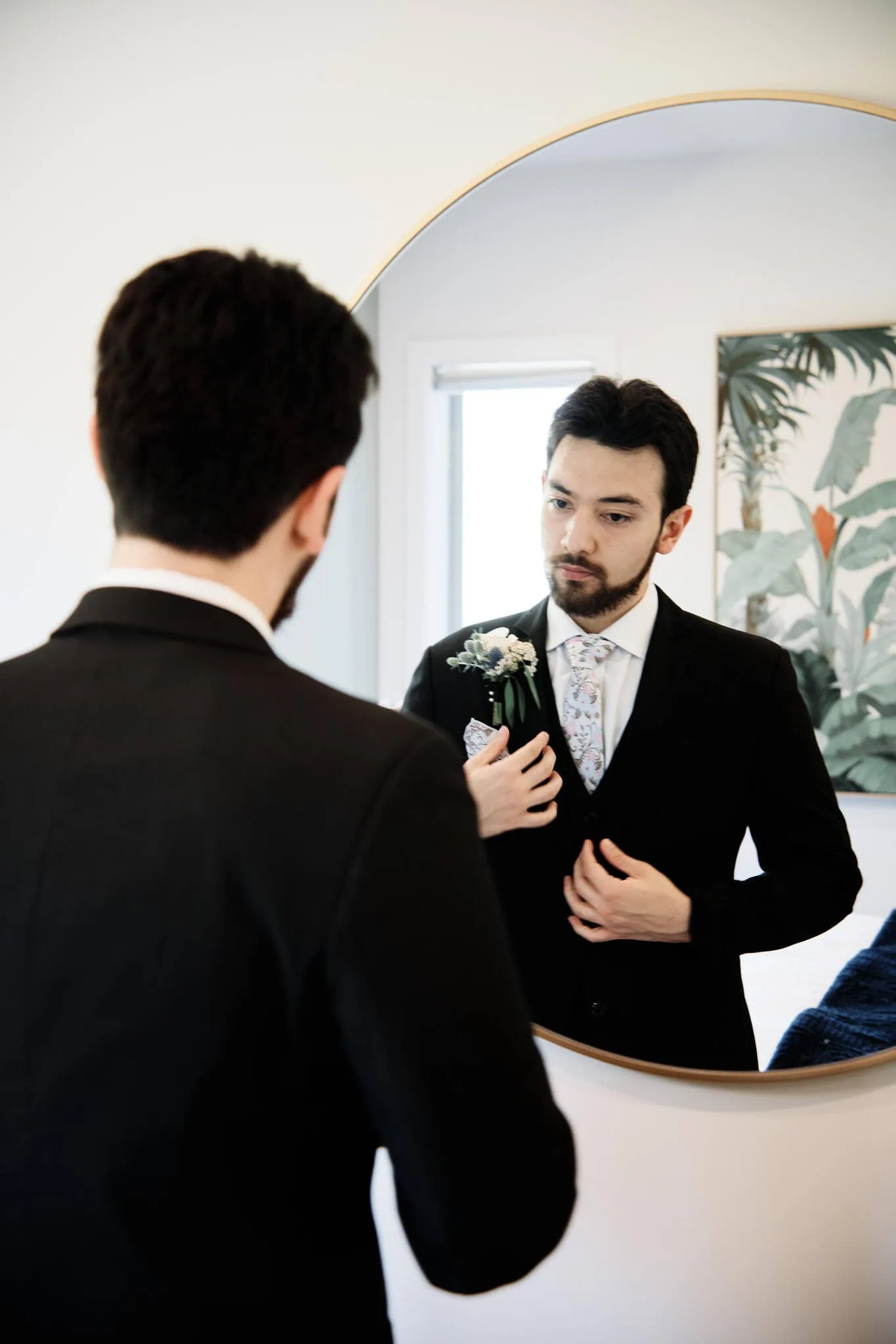 Carlos, wearing a suit, prepares in front of a mirror for an intimate Cecil Peak Heli Elopement Wedding.