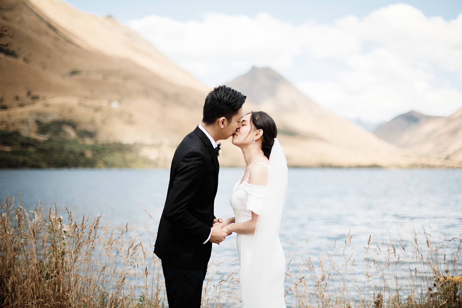 A bride and groom, Dios & Carlyn, share a romantic kiss at Cecil Peak in Queenstown during their Heli Pre Wedding shoot.