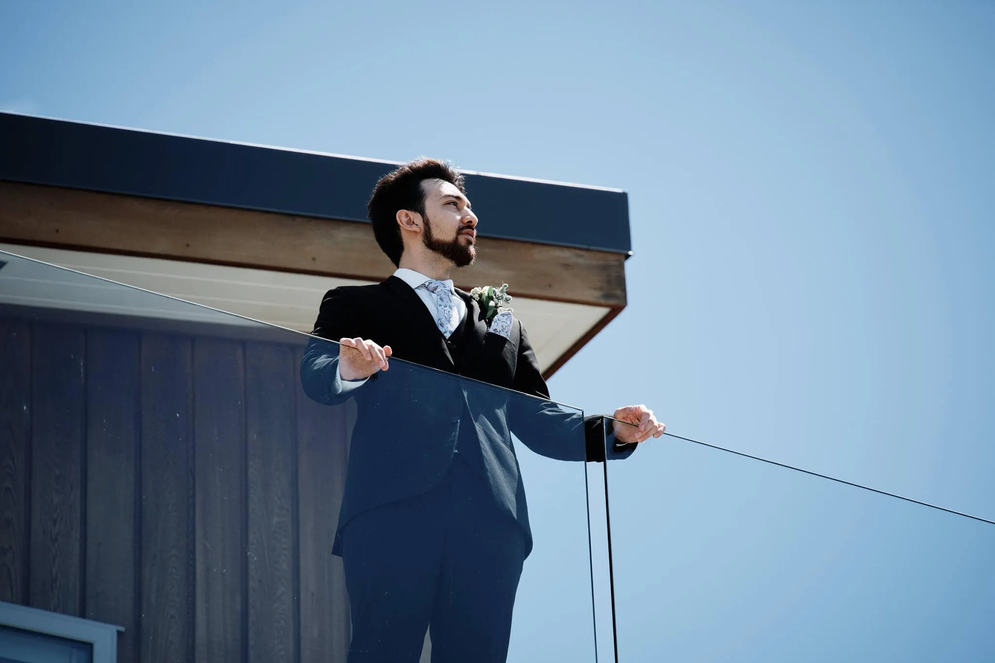 A man in a suit standing on a balcony during an intimate Cecil Peak heli elopement wedding.