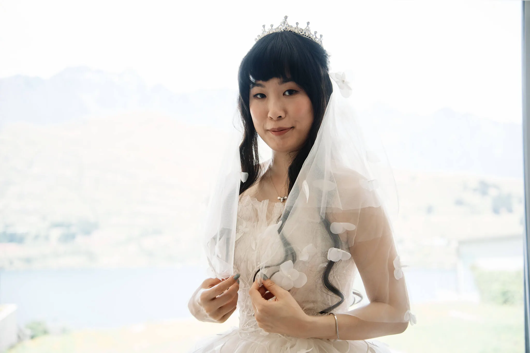 Carlos and Wanzhu's intimate Cecil Peak Heli Elopement Wedding, with a bride in a wedding dress posing in front of a window.