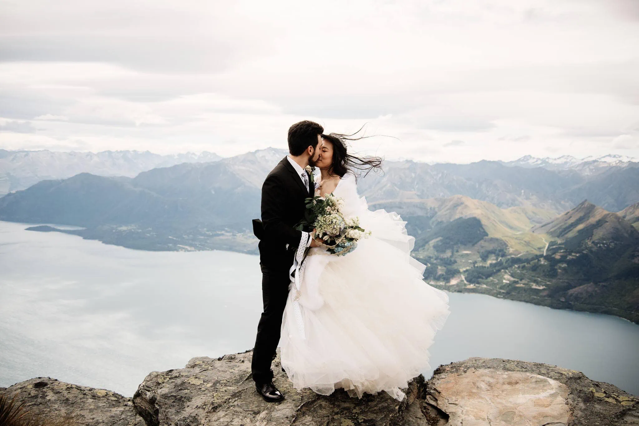 Carlos and Wanzhu share an intimate kiss on top of Cecil Peak, overlooking Lake Wanaka during their heli elopement wedding.