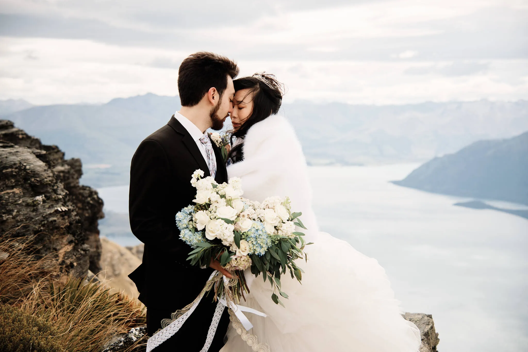 Carlos and Wanzhu celebrate an intimate heli elopement wedding atop Cecil Peak, sharing a kiss overlooking Lake Wanaka.