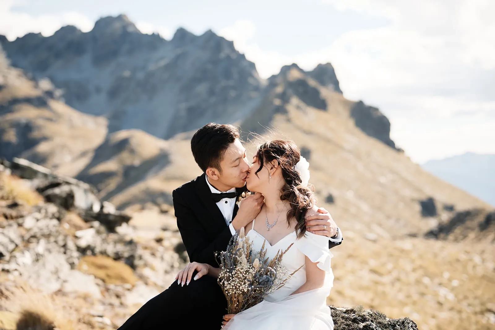 Dios and Carlyn, a bride and groom, share a passionate kiss atop Cecil Peak during their Queenstown heli pre-wedding photoshoot in New Zealand.