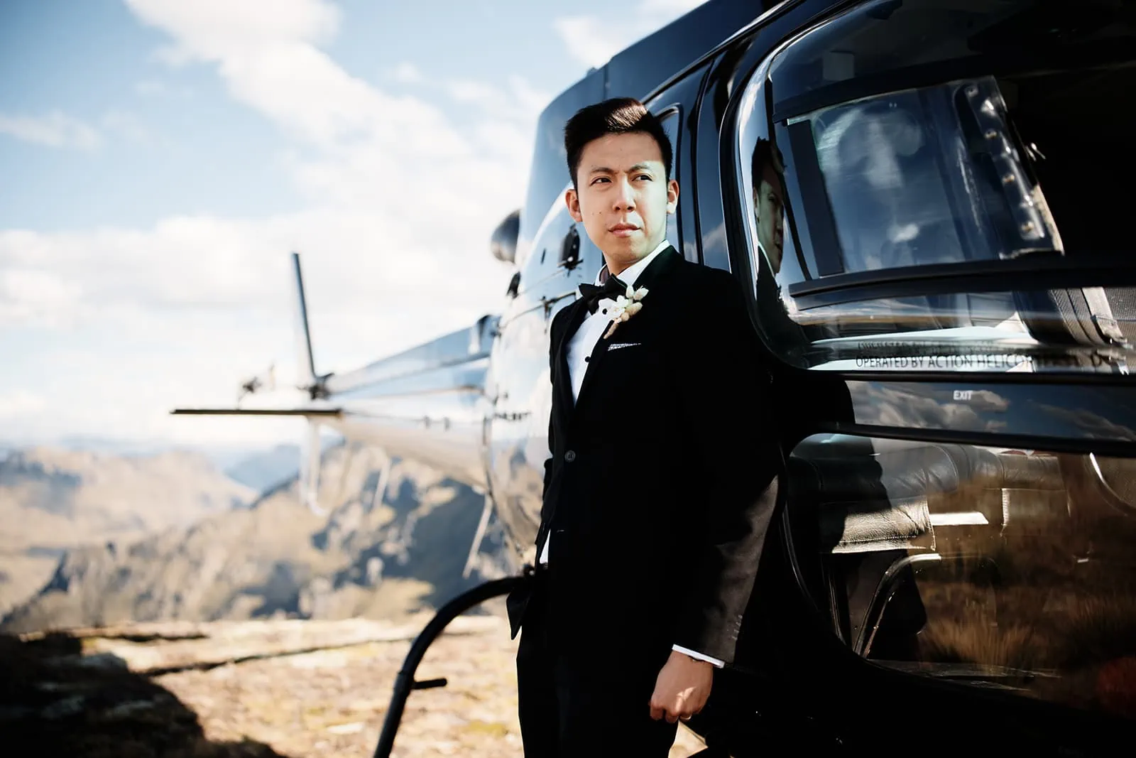 A man in a tuxedo standing next to a helicopter during the Queenstown Heli Pre Wedding at Cecil Peak.