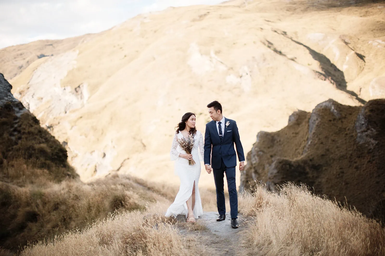 A bride and groom in Queenstown, standing on a path at Cecil Peak during their Dios & Carlyn Queenstown Heli Pre Wedding shoot.