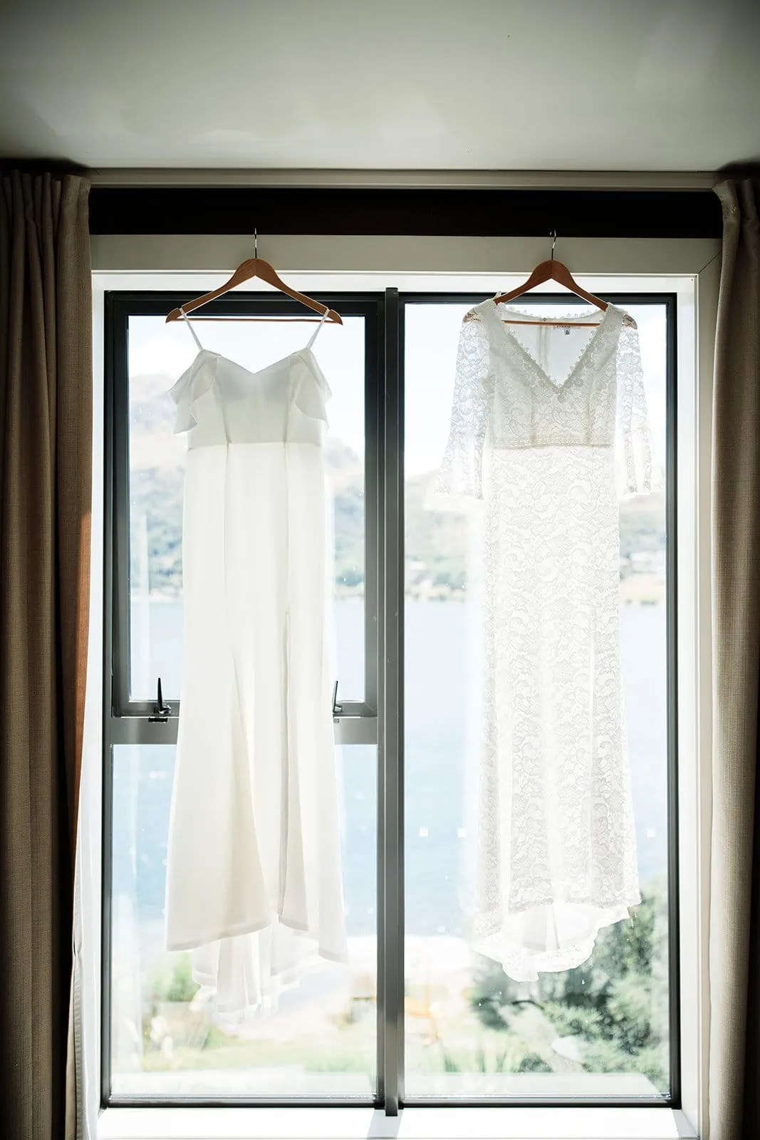 Dios & Carlyn's Queenstown Heli Pre Wedding: Two wedding dresses hanging from a window in a room at Cecil Peak.