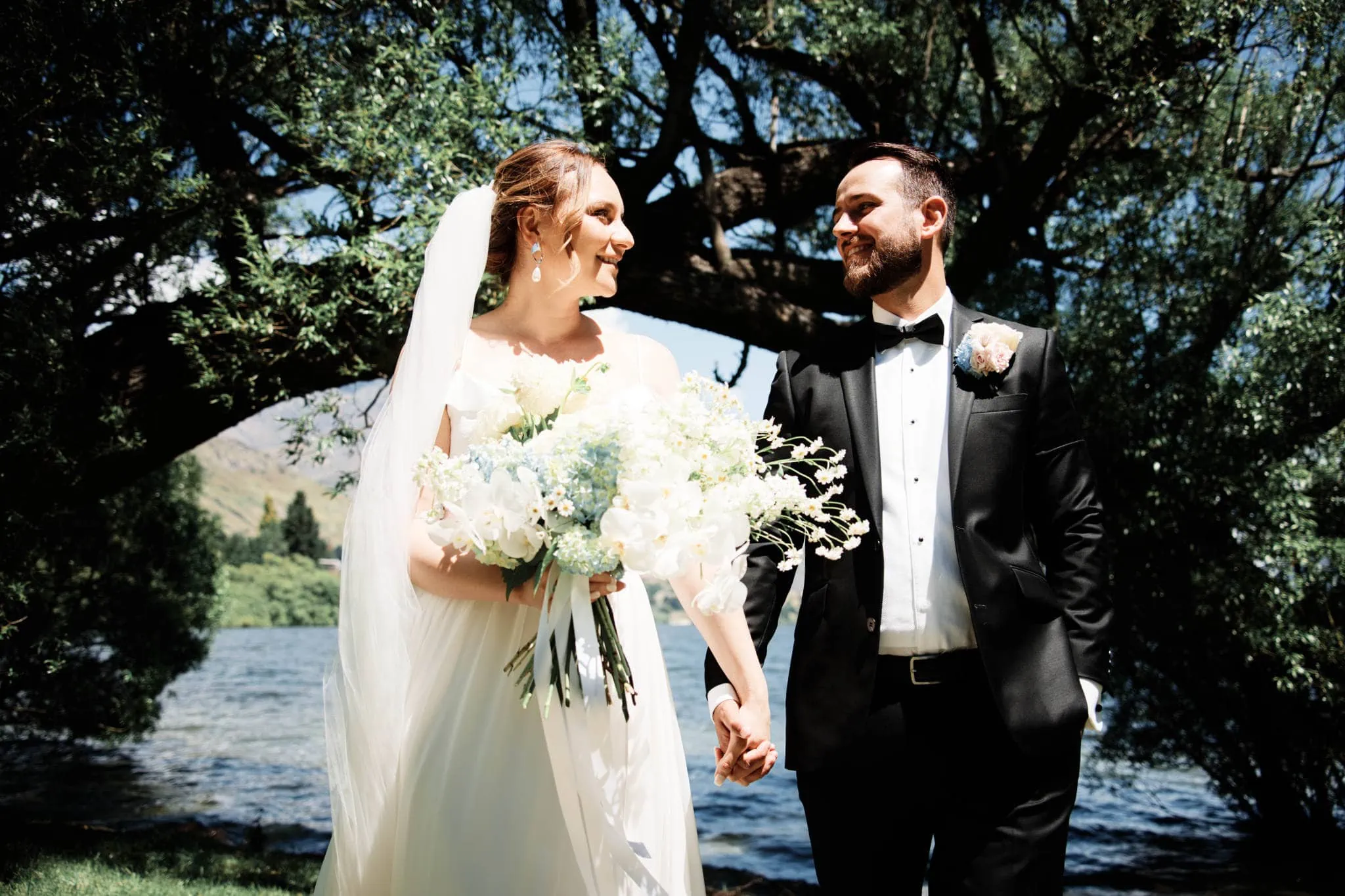 A Sapphire and JJ eloping in Queenstown, holding hands in front of a lake for their heli wedding.