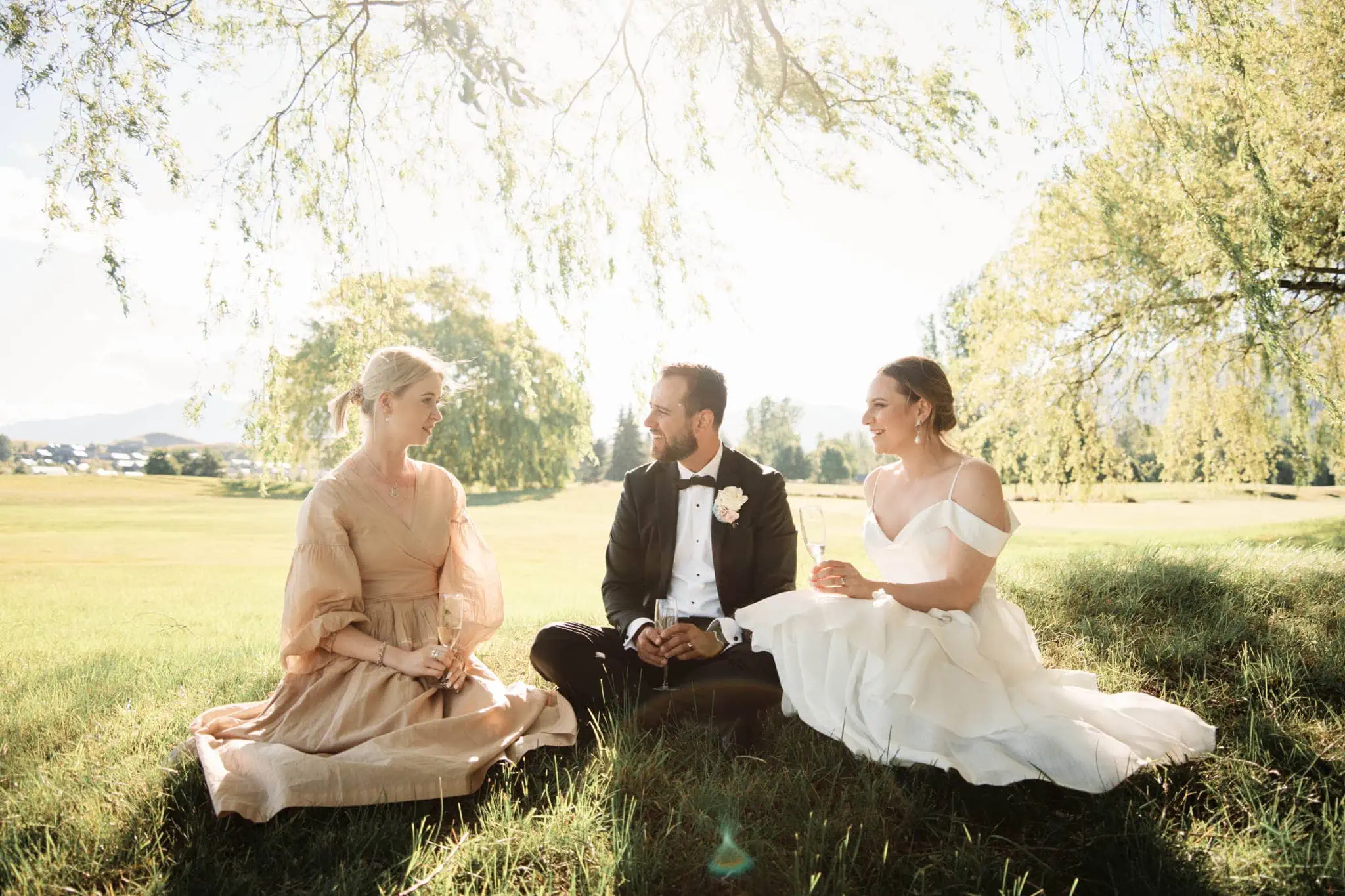 Sapphire and JJ exchange vows during their Queenstown Heli Elopement Wedding, seated on the grass in front of a tree.