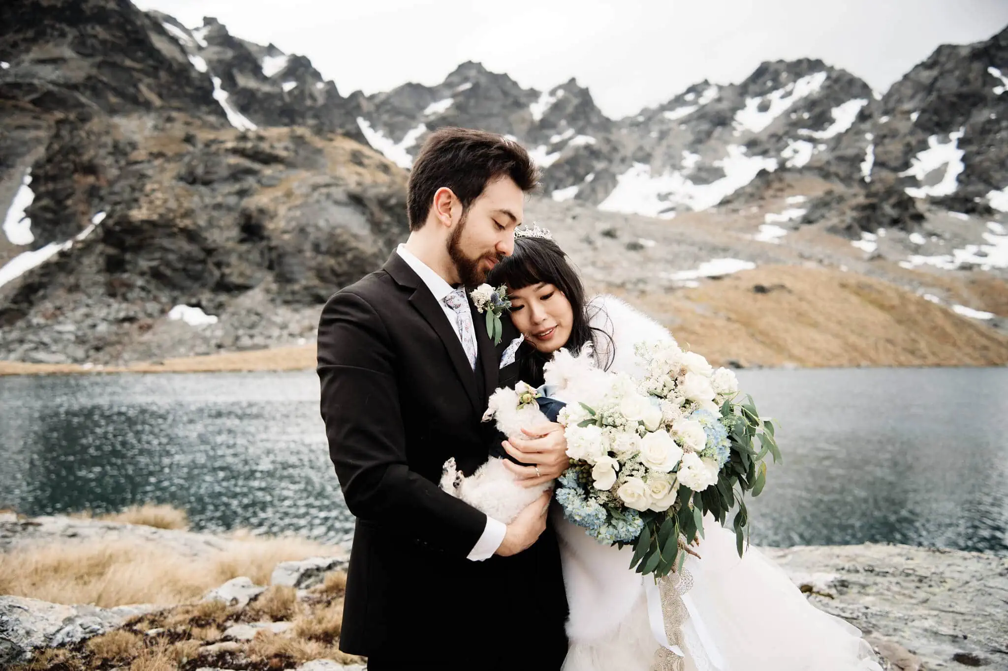 Carlos and Wanzhu's intimate wedding elopement, holding their dog in front of a lake in the mountains at Cecil Peak.