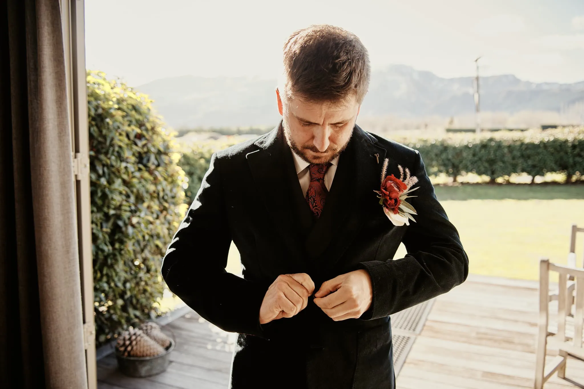 A man in a suit is adjusting his tie at Claire and Rob's heli elopement wedding at Cecil Peak.