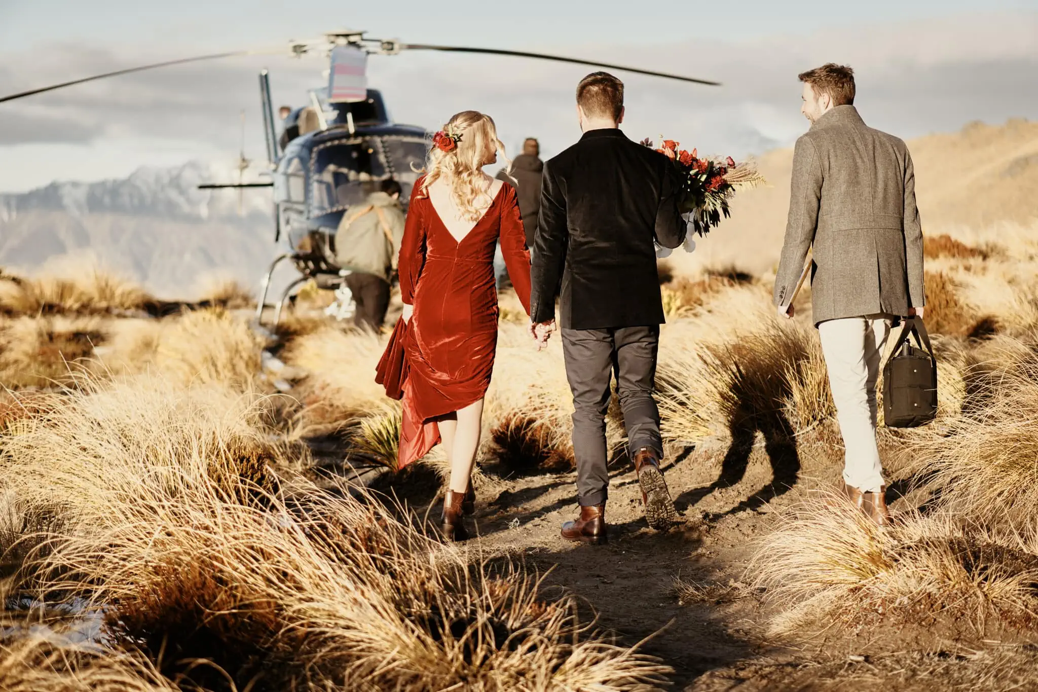 Claire and Rob's Heli Elopement Wedding at Cecil Peak captures them walking down a path with a helicopter in the background.