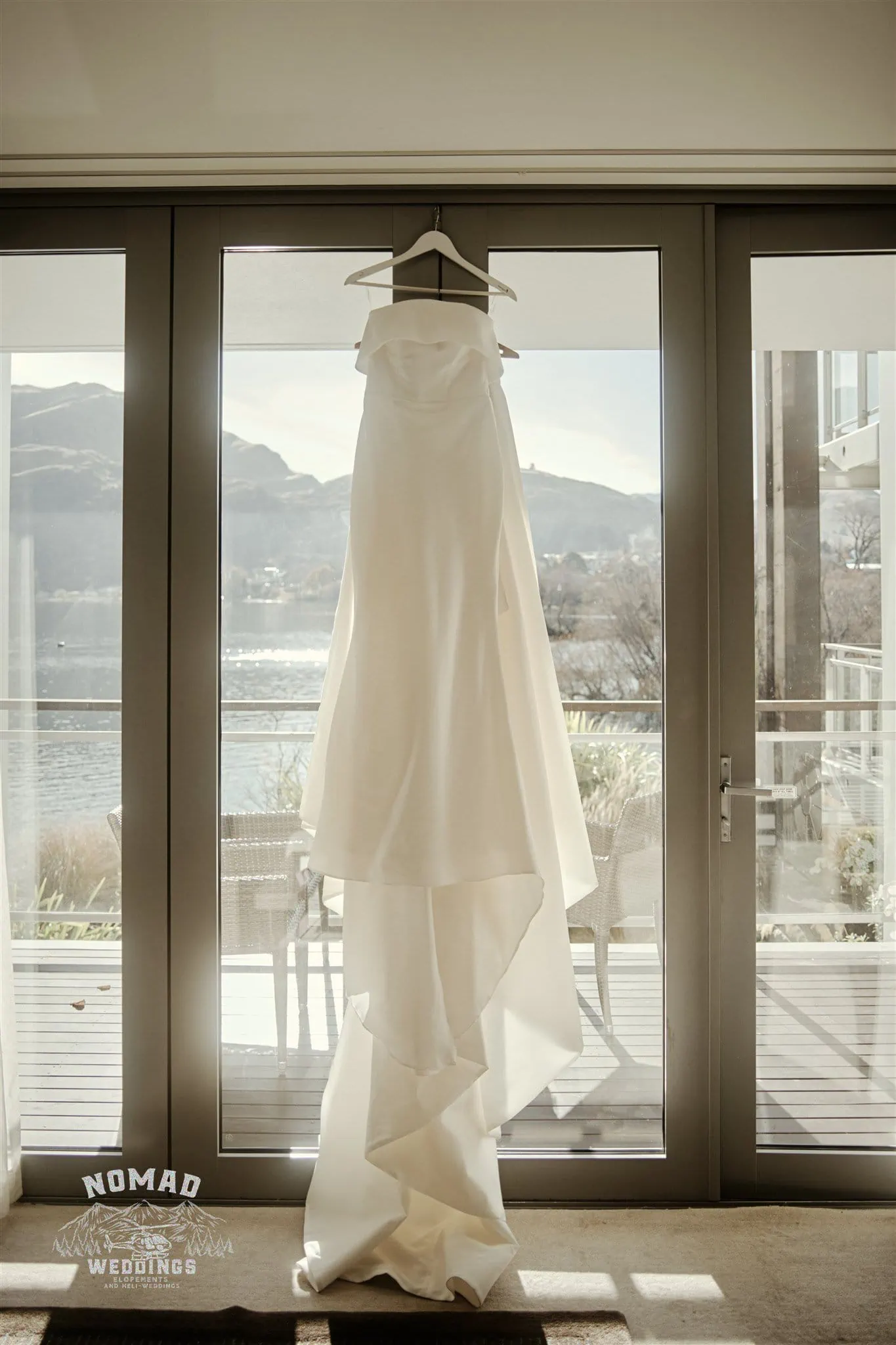Jay and Dave's wedding dress hangs in front of a window overlooking Coromandel Peak.