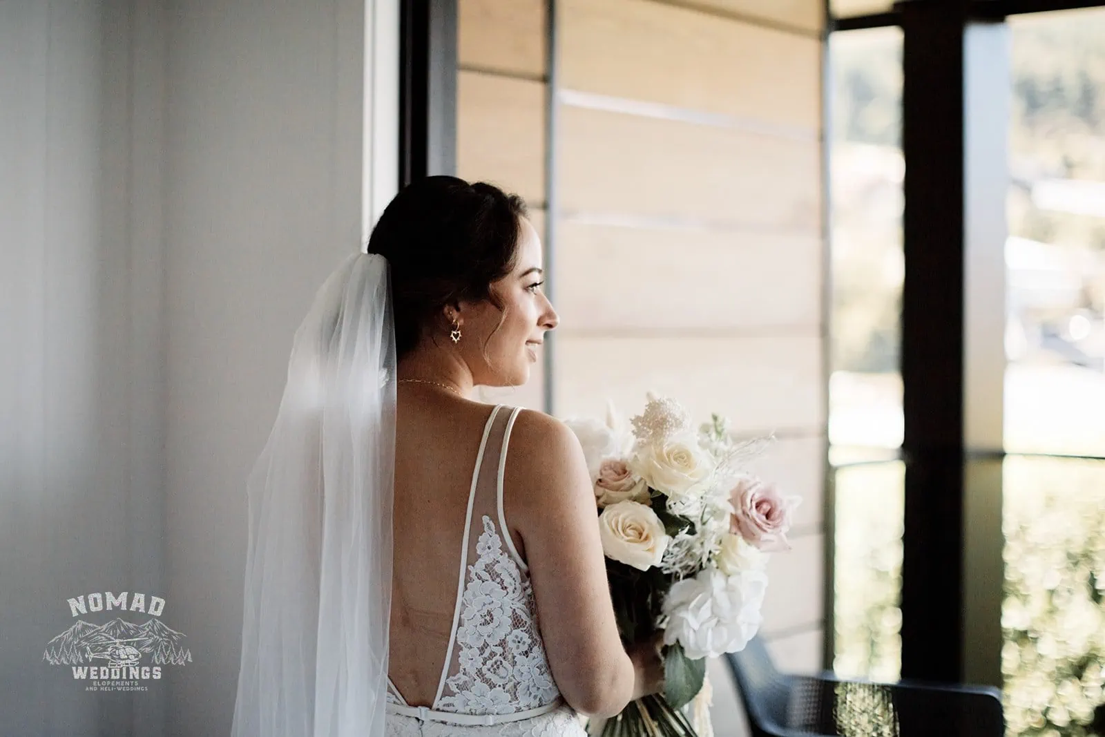 Amy looking out of window with her bouquet at Enchanting Lake Erskine Heli Elopement Wedding.