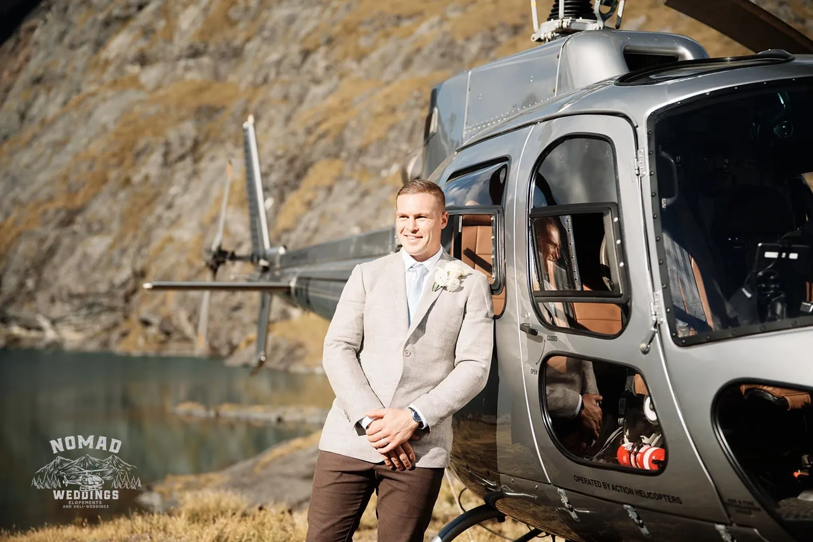 An enchanting groom stands in front of a helicopter at Amy & Eden's Lake Erskine heli elopement wedding.