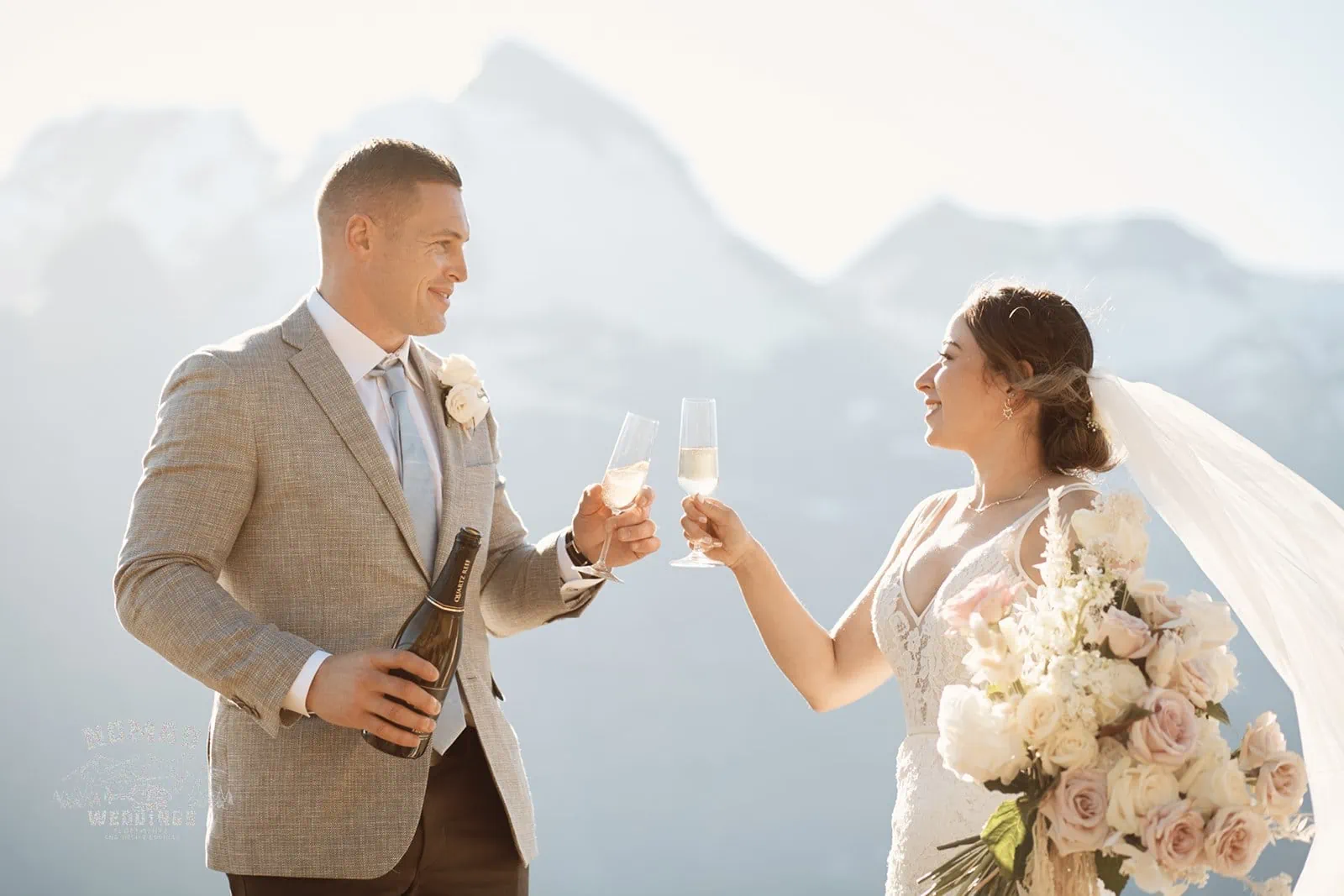Amy & Eden toasting champagne in front of mountains at their enchanting Lake Erskine heli elopement wedding.